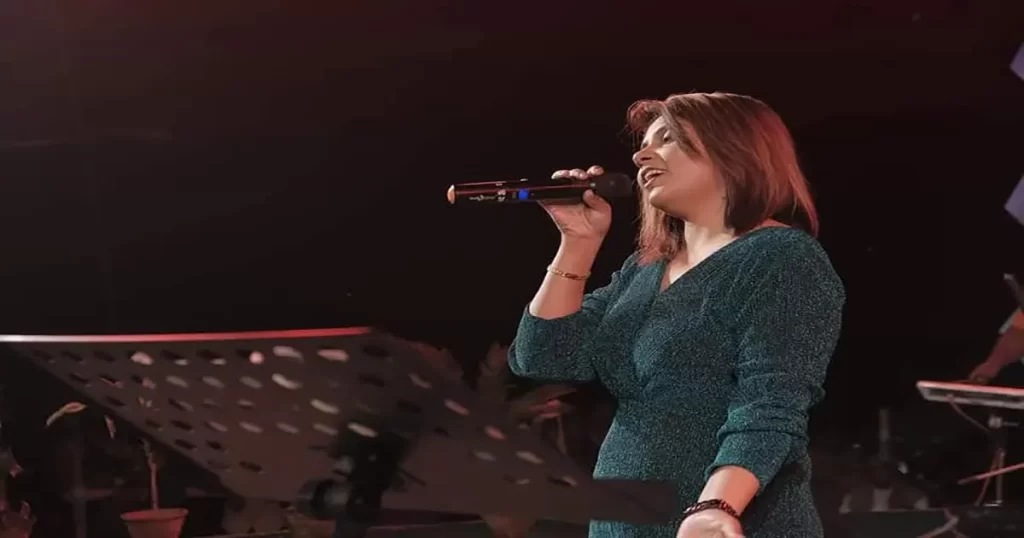 Madhumita Chakraboty passionately performing on stage with a microphone, representing the expressive training and performance opportunities offered in a vocal music class.